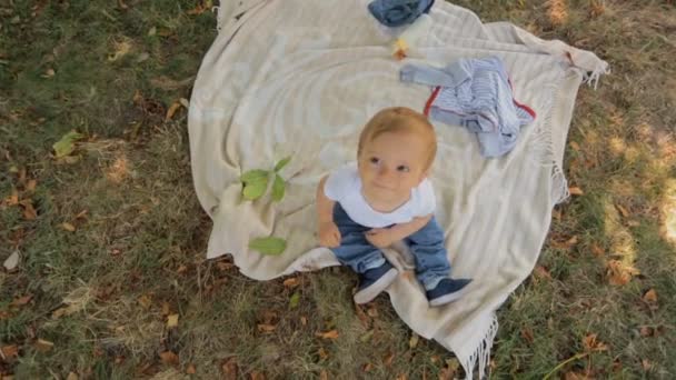 Portrait de mignon bébé garçon souriant assis sur la couverture sous l'arbre au parc 