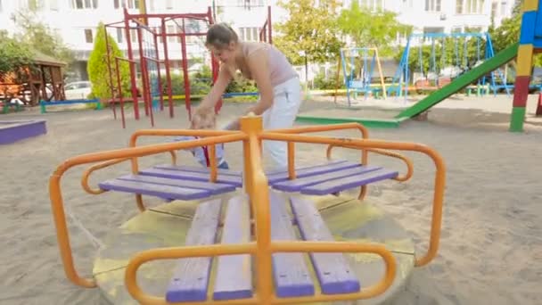 Schattige lachende babyjongen draaien carrousel op speelplaats — Stockvideo