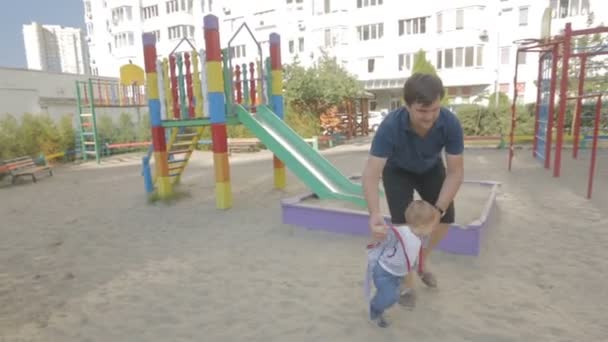 Glad ung man promenader med sin baby son lekplatsen — Stockvideo