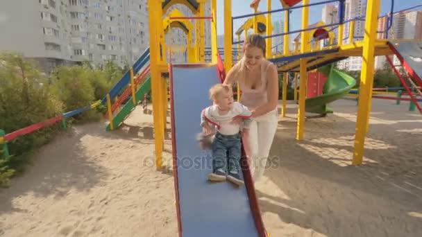 Веселый 1-летний мальчик, катающийся на горке на детской площадке — стоковое видео