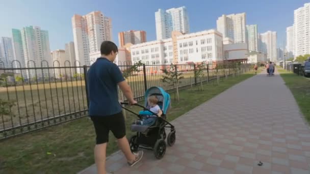 Χαρούμενος νεαρός πατέρας πιέζει καροτσάκι μωρού στην οδό ηλιόλουστη ημέρα — Αρχείο Βίντεο