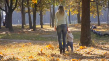 Genç anne bebek oğlu ile sonbahar Park sarı yapraklar üzerinde yürüyen