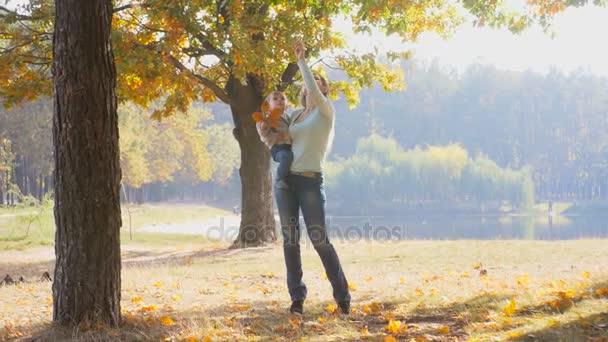 Beautiful young mother reaching for the leaf on tree and giving it to her baby son — Stock Video