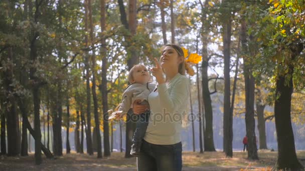 幸せな若い母彼女の赤ちゃんの息子を抱いて、彼に示すのスローモーション映像が木に葉します。 — ストック動画