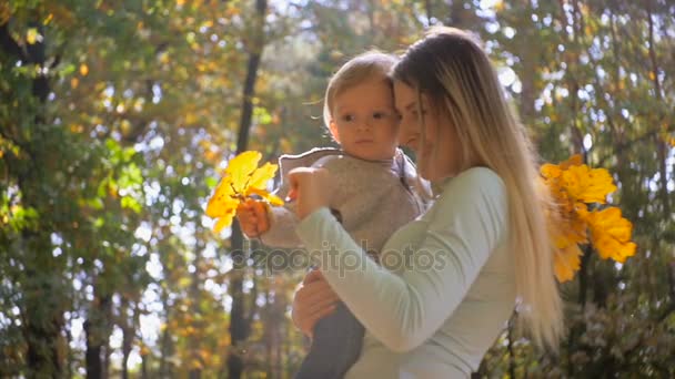 Imágenes en cámara lenta del lindo bebé y la madre jugando con hojas en el parque de otoño — Vídeos de Stock