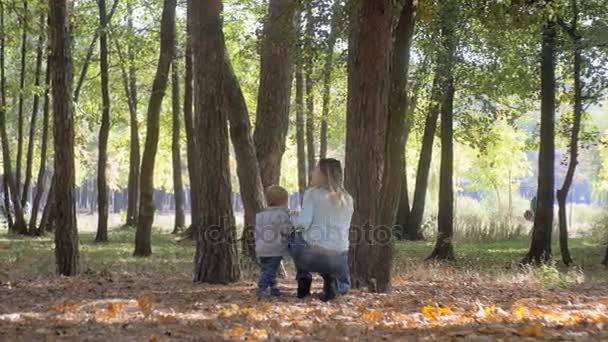 Glad ung mamma med att titta på höstträd på park med sin baby son — Stockvideo