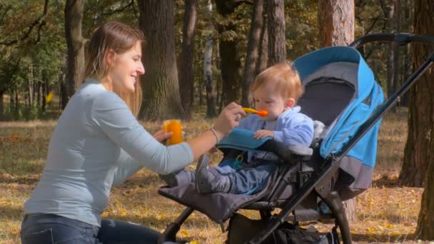 4K metraje de lindo bebé niño sentado en cochecito en el parque y comer salsa de manzana — Vídeo de stock