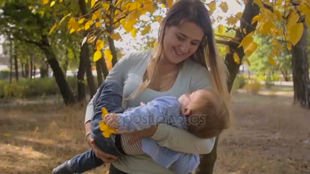 Film al rallentatore di felice giovane madre che abbraccia e gira suo figlio al parco — Video Stock