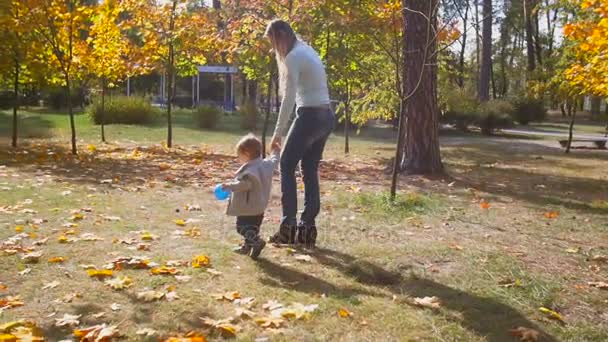 Feliz madre sosteniendo a su hijo bebé y caminando en el parque de otoño — Vídeos de Stock