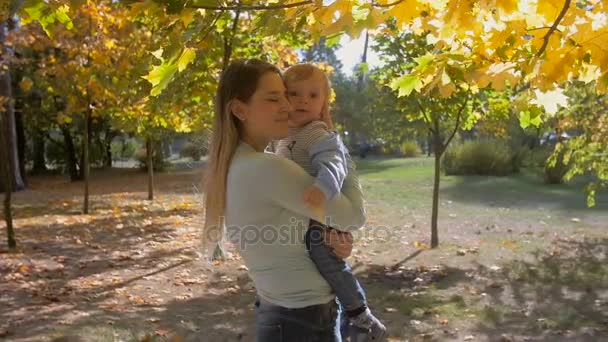 Retrato en cámara lenta de la madre abrazando a su hijo bebé bajo el árbol en el parque de otoño — Vídeos de Stock