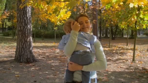 Images au ralenti de la belle mère attentionnée embrassant son bébé fils au parc d'automne sous un grand arbre 