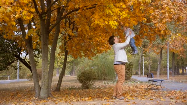 Imágenes en cámara lenta de feliz padre y bebé divirtiéndose en el parque de otoño — Vídeo de stock