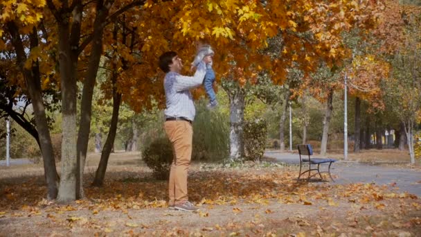 Imágenes en cámara lenta de feliz padre joven lanzando a su hijo en el parque de otoño — Vídeos de Stock
