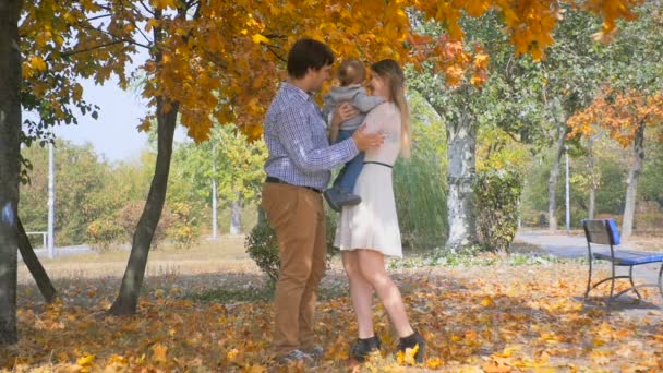 Filmagem em câmera lenta de um jovem feliz abraçando e beijando sua família no parque de outono — Vídeo de Stock