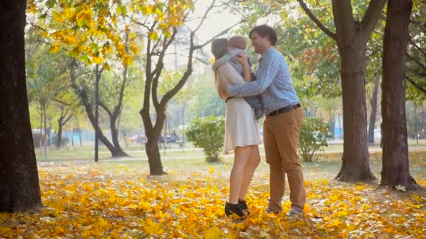 Imágenes en cámara lenta del joven feliz abrazando a su esposa y su bebé en el parque de otoño — Vídeos de Stock