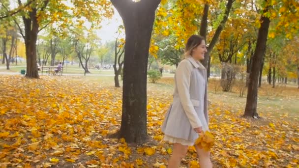 Slow motion steadicam footage of beautiful smiling woman walking at autumn park — Stock Video