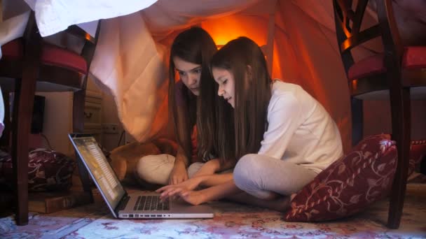 Due ragazze in pigiama utilizzando il computer portatile a casa fatta di coperte di notte — Video Stock