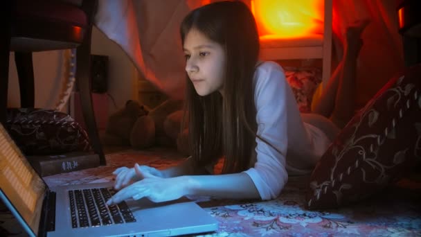 4k dolly disparo de linda chica en pijama acostado en el suelo en el dormitorio y escribir en el ordenador portátil por la noche — Vídeos de Stock