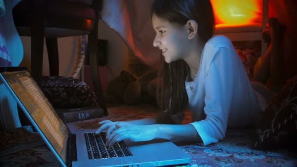 Linda chica sonriente en pijama usando computadora portátil en tienda de campaña tipi por la noche — Vídeo de stock