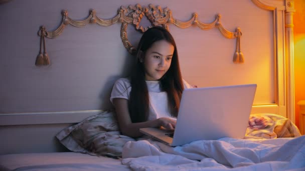 아름 다운 웃는 여 자가 침대에 누워 및 채팅 노트북에 밤에의 4 k 비디오 — 비디오