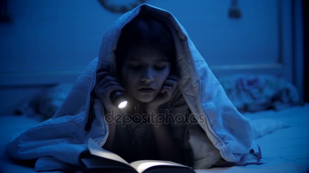Χαριτωμένο κορίτσι κάτω από την κουβέρτα στο κρεβάτι ανάγνωση του βιβλίου — Αρχείο Βίντεο
