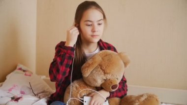 Kulaklık ile müzik dinlemek ve oyuncak ayı sarılma genç kız ağır çekim görüntüleri