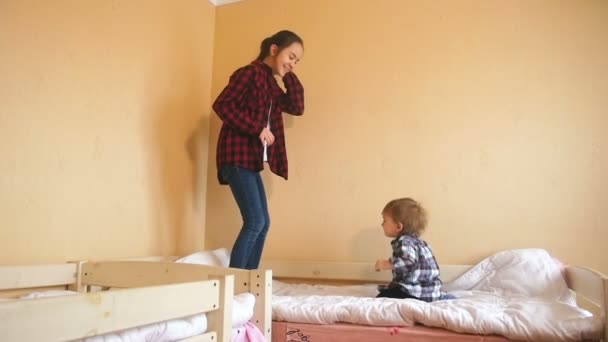 Zeitlupenaufnahmen von Teenager-Mädchen, die mit Baby-Junge auf Bett springen — Stockvideo