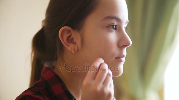 Closeup slow motion footage of sad teenage girl putting earphones in ears and looking out of window — Stock Video