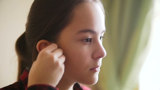 Vértes videó a tizenéves lányok fülhallgatóval zenét hallgatni, és néz ki az ablak — Stock videók