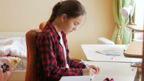 4k кадров, где сконцентрированная девочка-подросток делает домашнее задание за столом в спальне — стоковое видео
