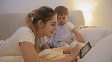 Yatakta yatan ve tablet bilgisayar kullanarak yürümeye başlayan çocuk ile anne