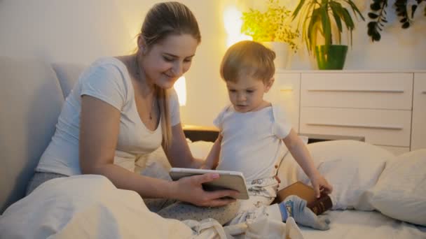母亲与婴儿在床上的平板电脑享受收看视频的 4 k 镜头。 — 图库视频影像