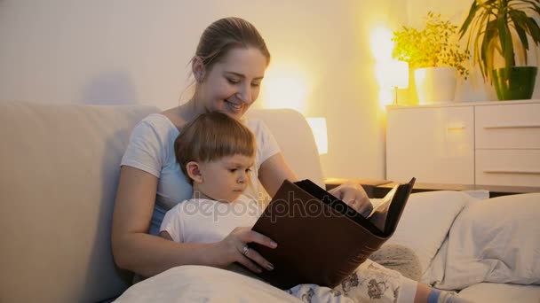 母亲阅读本书给她的宝贝儿子在床上的 4 k 镜头。 — 图库视频影像