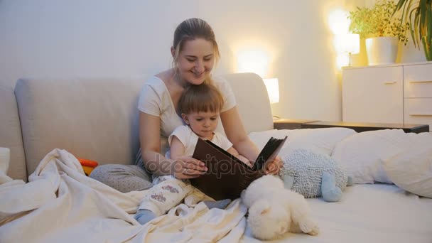 Young mother with baby lying in bed and watching family photo album — Stock Video