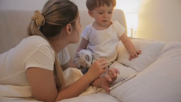 Lindo bebé niño mirando a la madre usando tableta digital en la cama por la noche — Vídeo de stock