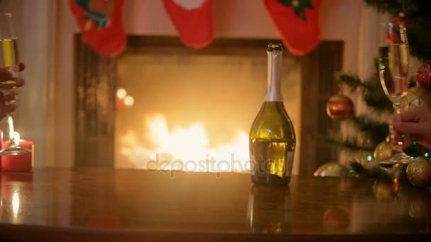 Hands of couple in love clinking glasses with champagne at Christmas eve. Man and woman sitting at burning fireplace at decorated living room. — Stock Video