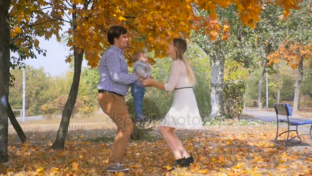 Медленная съемка счастливой молодой пары, обнимающей и играющей со своим маленьким сыном в осеннем парке — стоковое видео