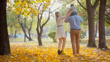 Mutlu aile sonbahar Park babalar omuzlarında oturan bebek oğlum ile yürüme ağır çekim görüntüleri