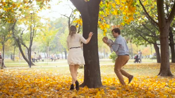 Imágenes en cámara lenta del feliz padre joven sosteniendo al bebé y corriendo tras la madre en el parque de otoño — Vídeos de Stock