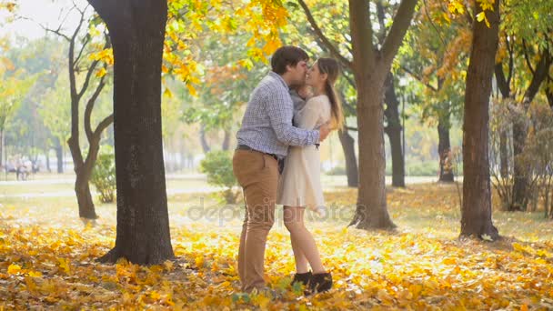 Imágenes en cámara lenta de padres jóvenes felices sosteniendo a su hijo bebé y besándose en el parque de otoño — Vídeo de stock