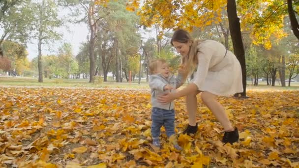 Filmato al rallentatore di adorabile bambino che fa i primi passi con la madre al parco autunnale — Video Stock
