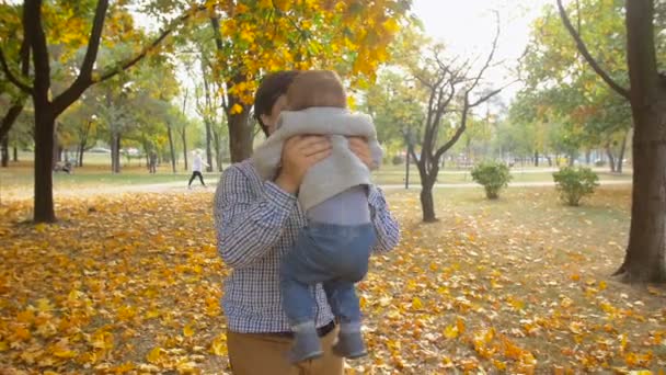 Filmagem em câmera lenta do jovem pai feliz segurando e girando com seu filho bebê no parque de outono — Vídeo de Stock