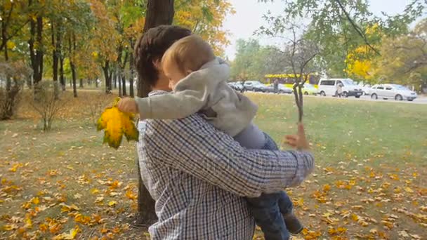 Retrato en cámara lenta de un joven padre sonriente abrazando y girando a su hijo en el parque de otoño — Vídeos de Stock