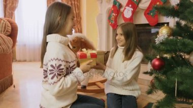 Oturma odası katında oturan ve her diğer Noel hediyeleri veren iki neşeli kız portresi