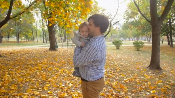 Slow motion beelden van gelukkige jonge vader houden teder zijn zoontje in herfst park — Stockvideo