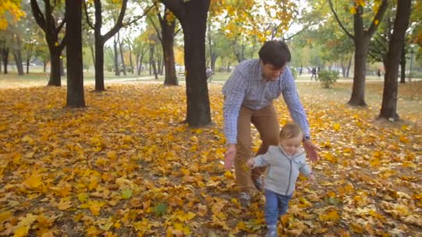 Filmagem em câmera lenta de pai carinhoso segurando seu filho bebê que caiu no parque de outono — Vídeo de Stock