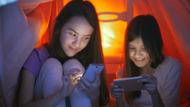 4 k-video av två söta leende flickor sitter under filt på natten och använda mobiltelefoner — Stockvideo
