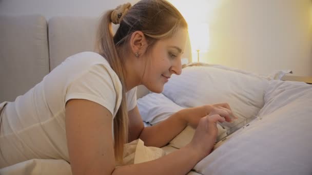 Bella donna sorridente sdraiata a letto e digitare il messaggio nei social media — Video Stock