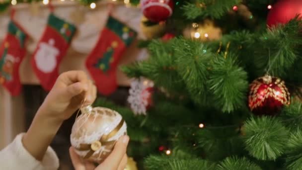 Closeup of girl in sweater hanging golden bauble on Christmas tree — Stock Video