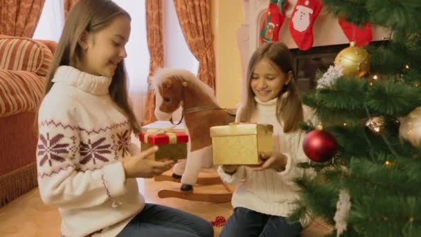 Two cheerful girls giving Christmas presents to each other and opening them — Stock Video